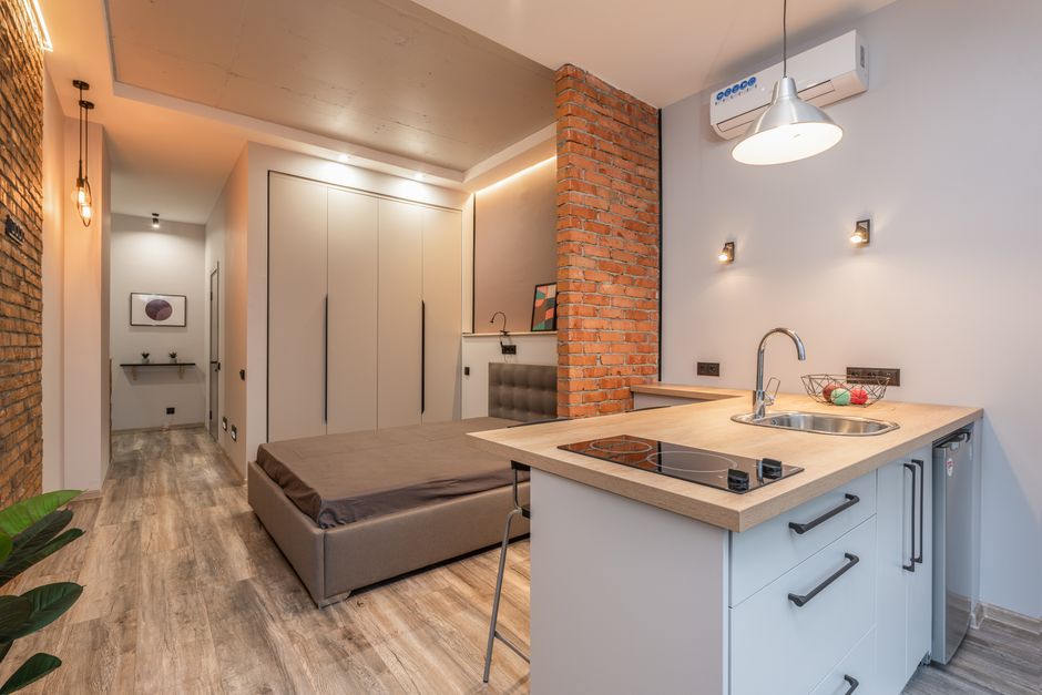 Miniature kitchen with modern appliances and bedroom behind brick partition in small loft style apartment